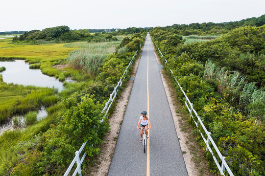 Aerial drone of Woman biking through Cape Cod Marshes bike path