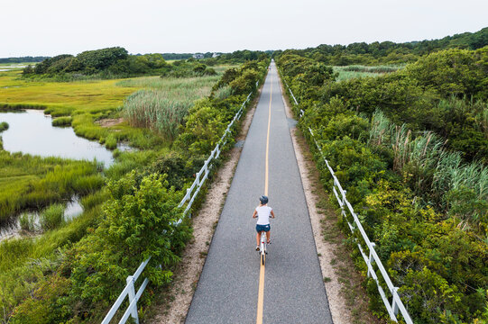 Aerial drone of Woman biking through Cape Cod Marshes bike path