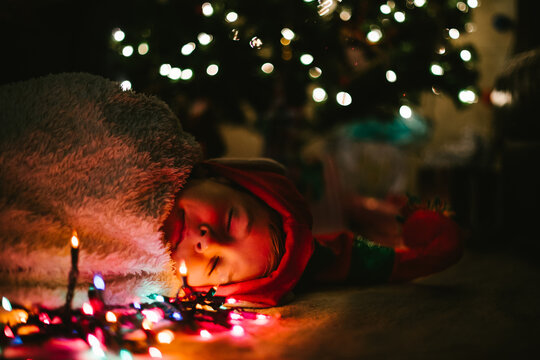 Boy child sleeps in cozy blanket and elf hat under Christmas tree