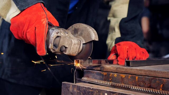 Sparks fly from under cutting disc angle grinder. Close-up of the master in work gloves with a grinder sawing off the profile on the desktop in the workshop.