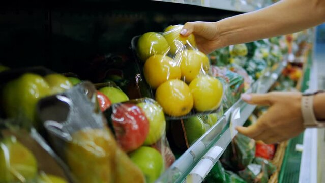 Close-up of a woman's hands choosing packaged apples on a supermarket counter.