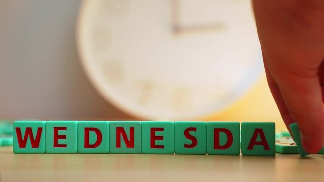 The word WEDNESDAY made of square colorful letters on the table with a time clock on the background. High quality 4k footage