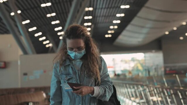 Young female traveler with tiket and mask in airport walking hall, view of tourist with backpack crossing terminal for registration