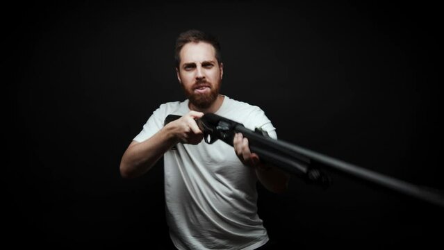 Close-up: a man holds a shotgun in his hands and aims looks at the camera