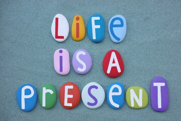 Life is a present, motivational message composed with multi colored stone letters over green sand