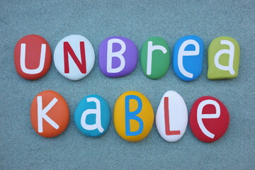 Unbreakable, creative text composed with multi colored stone letters over green sand