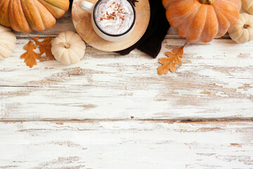 Cozy autumn top border with pumpkins, leaves, sweater and pumpkin spice latte. Overhead view over a rustic white wood background.