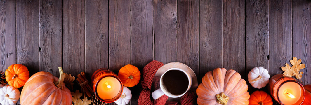 Cozy fall bottom border with pumpkins, sweaters, candles and coffee. Top view over a dark wood banner background.