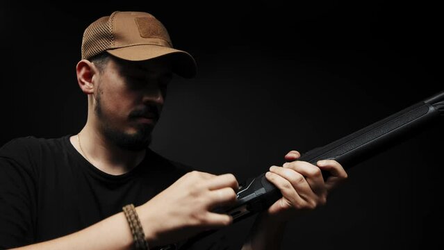Close-up: a man in a black T-shirt on a black background loads a shotgun