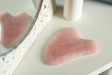 Rose quartz gua sha tool near mirror on white table, closeup