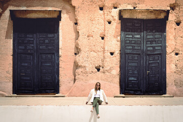 mujer sentada frente a una vieja construcción de grandes puertas. 