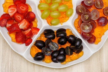 flatten view of a tray with fresh grapes of different colors and halved strawberries on orange jelly