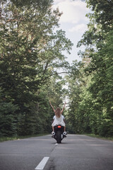 A young happy couple rides a motorcycle on an asphalt road in the forest, freedom and speed, backside