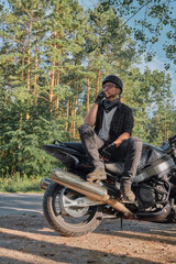 Young male biker in helmet travels on a motorcycle alone, stopped and smoking on the side of a forest road