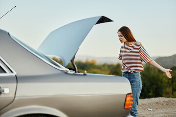 A woman sadly looks into the open trunk of a car during a stop on the road on the way to nature.