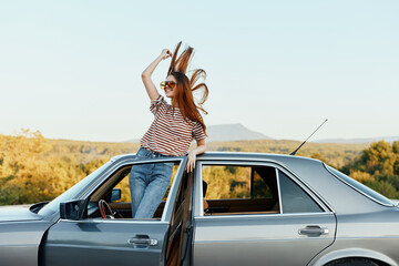 Happy woman traveler climbed on the car and spread her arms smiling happily. looks at the nature around. Lifestyle in travel and joy
