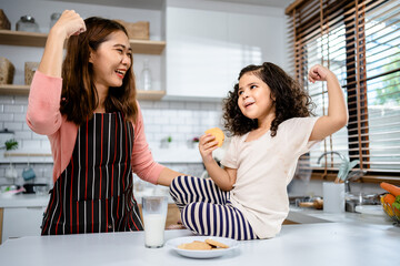 Mother with daughter having fun drinking milk with cookies together in the kitchen, relationships with learning development and leisure activities for children.