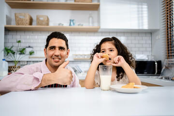 Father with daughter having fun drinking milk with cookies together in the kitchen, relationships with learning development and leisure activities for children.