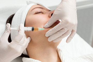 Cosmetologist gives an injection into the cheekbones of a young woman.. Doctor injecting hyaluronic...
