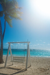 Dominican Republic, a beautiful beach with white sand and azure ocean. White beautiful swing for relaxing on the shore
