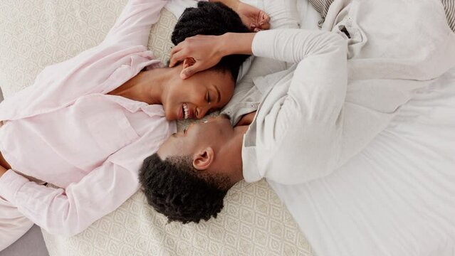 Love, black couple and kiss top view on their bed in the bedroom, hotel or house. Smile, romance and passion or happy dating man and woman bonding, loving or embracing in their home together.