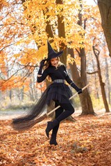 Naklejka premium Woman in witch costume standing in autumn forest on Halloween