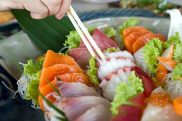 Closeup tako picking with chopsticks from mix sashimi set in ceramic plate. Japanese Cuisine...
