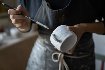 Experienced woman in black apron enjoys working with handmade craft in pottery studio. Female...