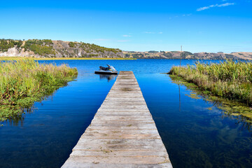 Fototapeta na wymiar Beautiful lake on a summer day and rustic wooden dock. Montains in blue sky.