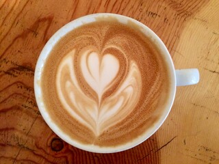 Latte in a mug with heart foam art on a wood table
