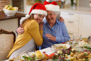 Caucasian woman and senior woman sitting at table and embracing