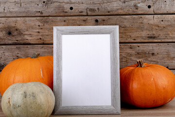 Composition of halloween decoration with pumpkins and frame with copy space on wooden background