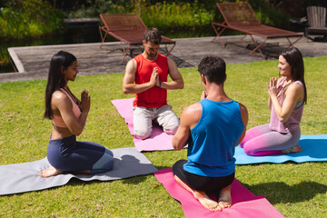 Men and women meditating on exercise mats in public park on sunny day