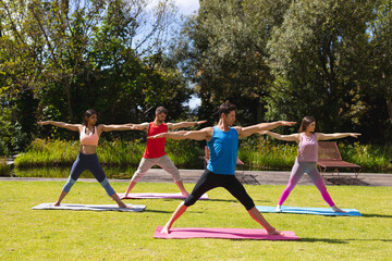 Full length of men and women practicing yoga on exercise mats in public park on sunny day