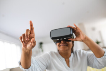 African american senior woman pointing while wearing virtual reality simulator at home, copy space
