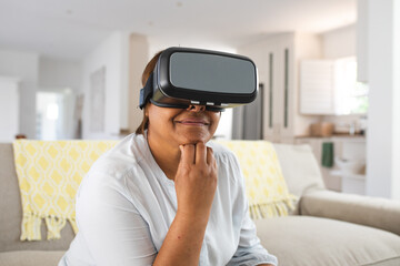 African american senior woman using wearing virtual reality simulator with hand on chin at home