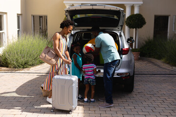 African american family loading luggage and ball in car trunk while going for picnic