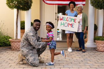 Happy african american family standing with placard while welcoming mid adult male soldier