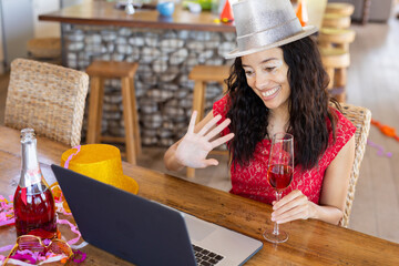 Smiling biracial young woman waving hand while enjoying party on video call over laptop at cafe - Powered by Adobe