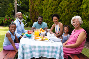 Portrait of smiling multiracial family sitting at breakfast table in backyard