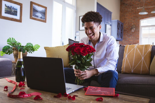 Happy young man holding fresh red rose bouquet during virtual date through laptop at home