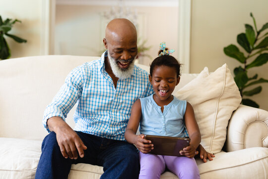 Smiling African American Senior Man With Granddaughter Using Digital Tablet While Sitting On Sofa