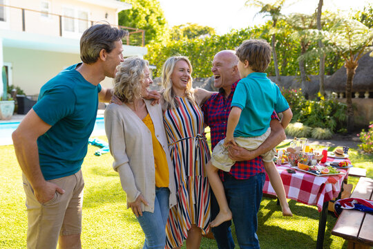 Cheerful caucasian family laughing while standing with arm around in backyard