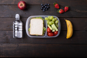 Overhead view of healthy food in lunch box by water bottle on wooden table, copy space