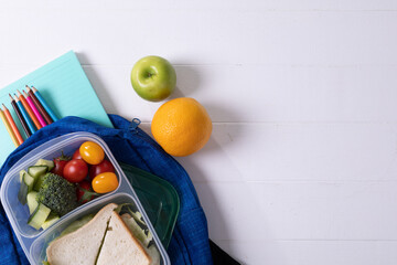 Directly above shot of healthy food and tiffin with school supplies on white background, copy space