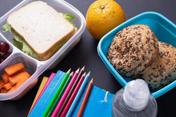 Healthy food and tiffin with school supplies on black background, copy space