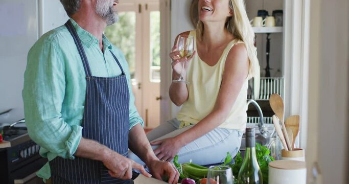 Happy caucasian mature couple cooking together and drinking wine in the kitchen