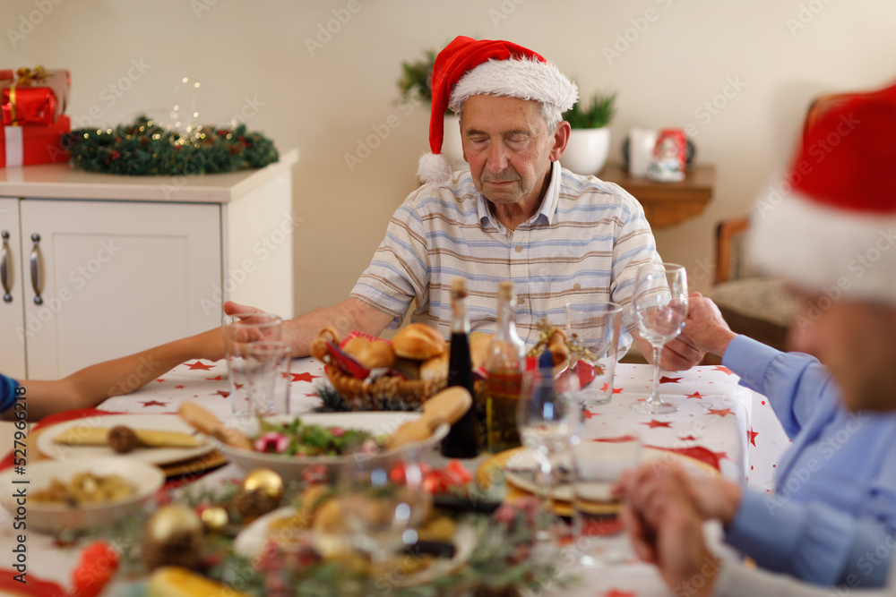 Wall mural multi generation caucasian family sitting at table and praying with eyes closed before dinner