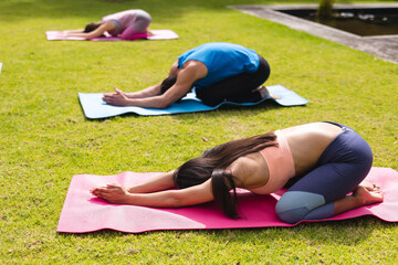 Women and man with hands clasped practicing yoga on exercise mats in public park