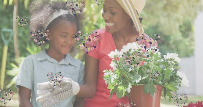 Animation of hearts over smiling african american mother and daughter gardening plants